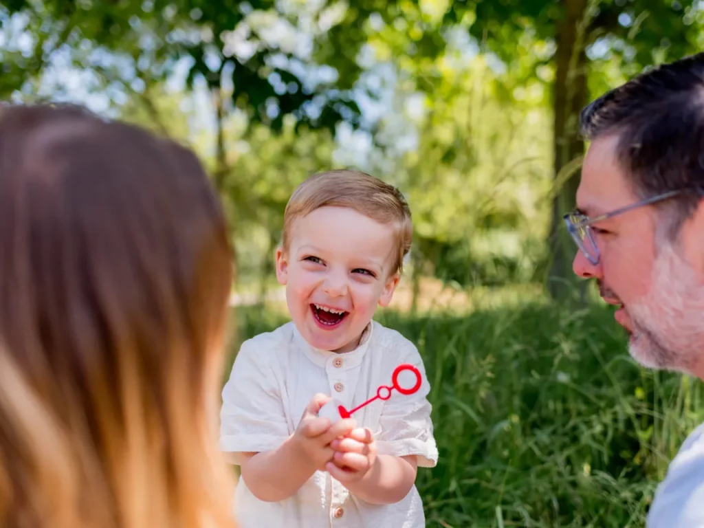 Kind spielt lachend mit Seifenblasen zwischen seinen Eltern bei einem Familienfotoshooting