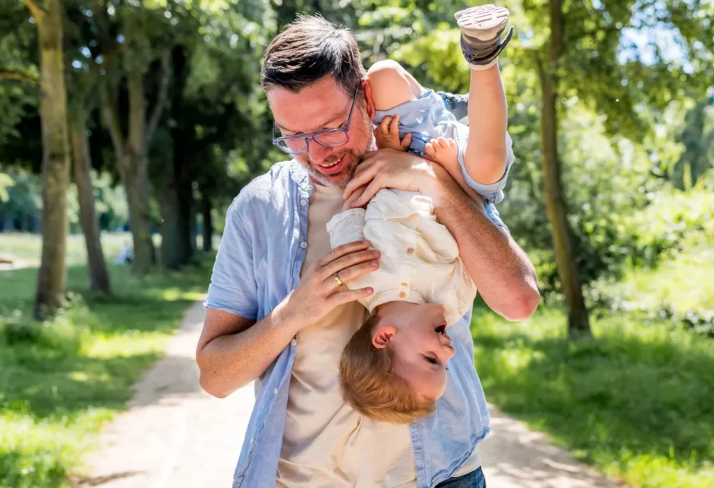 Vater spielt lachend mit seinem Kind bei einem natürlichen Familienfotoshooting im Park