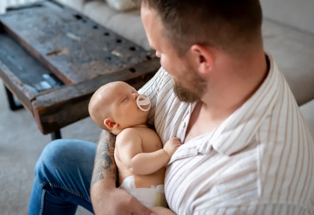Vater hält schlafendes Baby entspannt auf dem Arm im Wohnzimmer