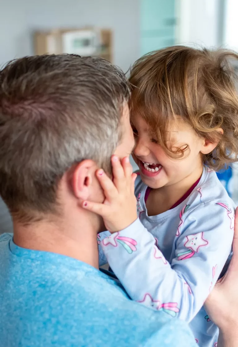 Kleines Kind lacht liebevoll im Arm eines Elternteils bei einem Familienshooting zuhause
