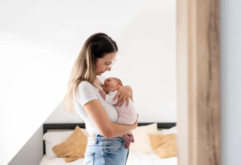 Mutter hält ihr schlafendes Baby ruhig im Arm in einem hellen Schlafzimmer