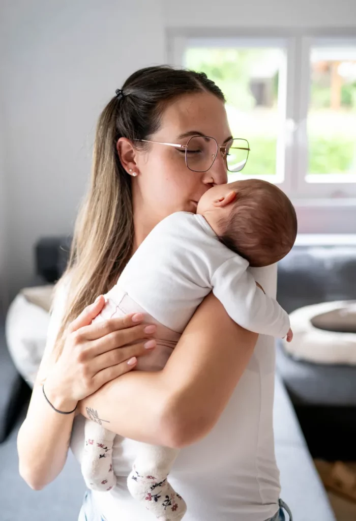 Mutter hält ihr Baby an der Schulter und küsst es in einem liebevollen Moment