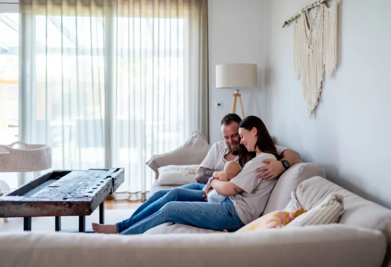 Eltern sitzen eng zusammen auf dem Sofa und halten ihr Baby im Arm