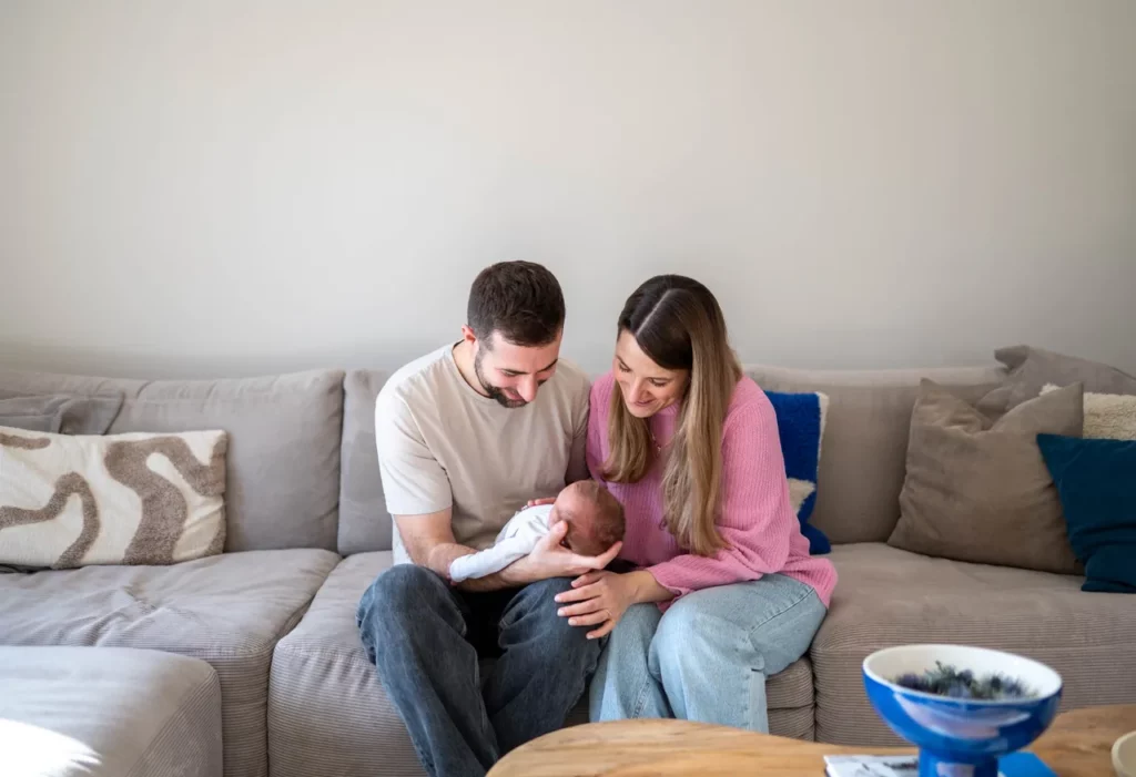 Eltern mit Baby auf dem Sofa in neutralen Tönen und rosa Strickpullover