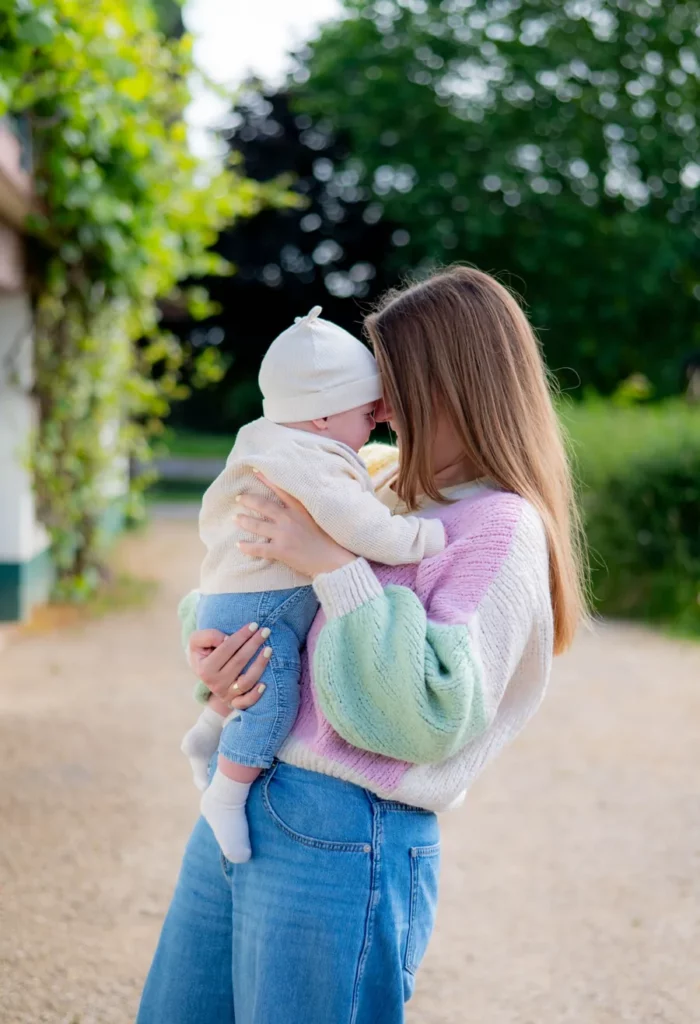 Mutter trägt groben Strick in Pastellfarben und hält ihr Baby draußen im Arm