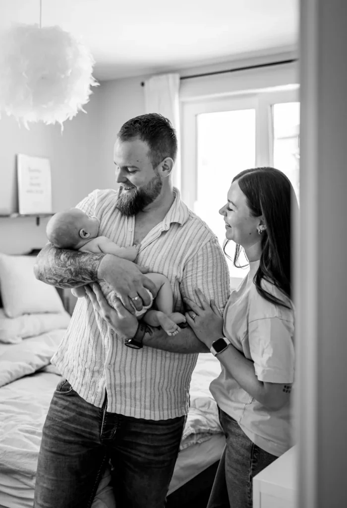 Eltern stehen gemeinsam im Schlafzimmer und schauen zu ihrem Baby im Arm des Vaters