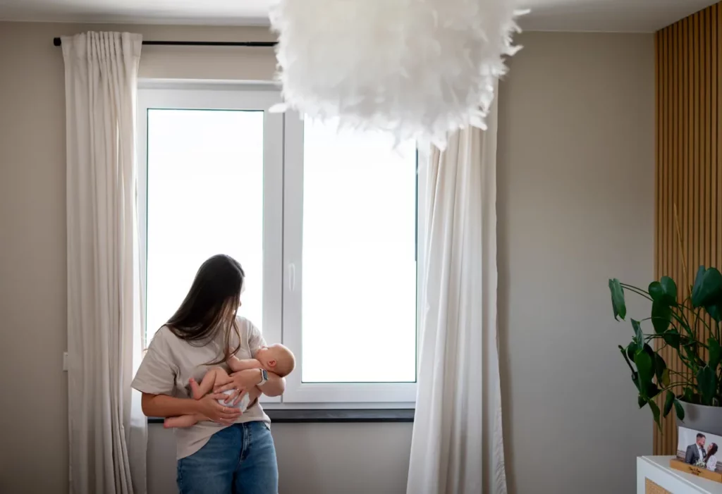 Mutter hält ihr Baby vor einem großen Fenster im Arm
