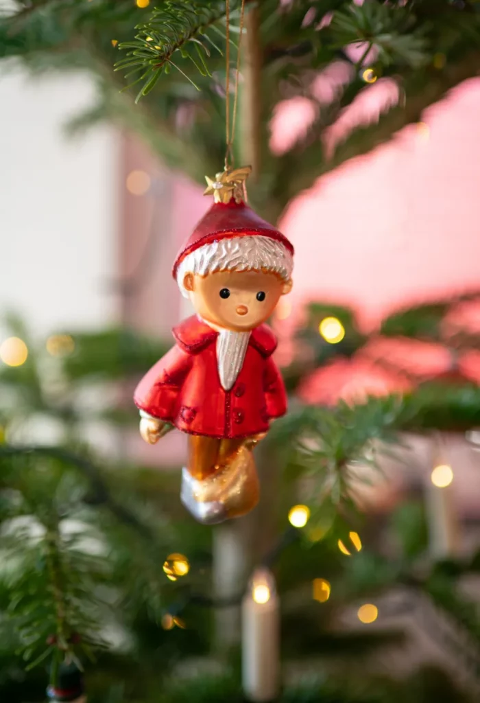 Kleine rote Figur als Baumschmuck zwischen Tannenzweigen