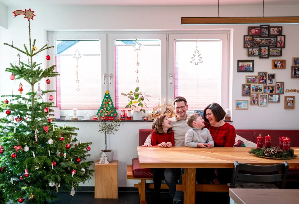 Familie mit zwei Kindern sitzt lachend neben dem geschmückten Weihnachtsbaum