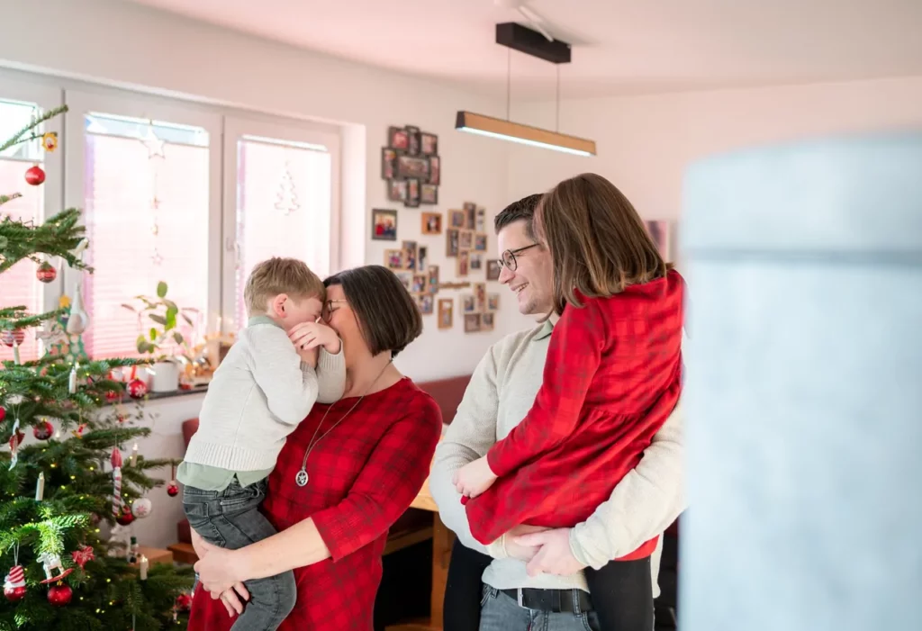 Familie mit zwei Kindern steht gemeinsam neben dem geschmückten Weihnachtsbaum