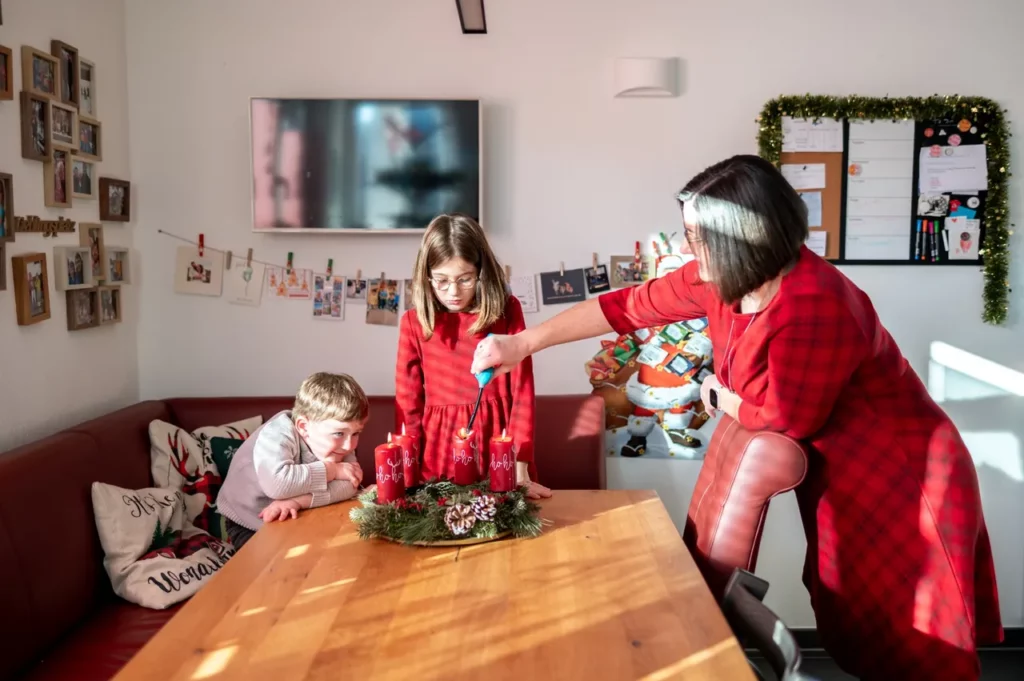 Frau und zwei Kinder stehen gemeinsam am Adventskranz