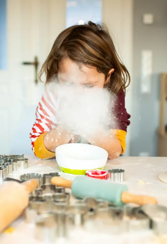 Kind pustet beim Backen eine Wolke aus Mehl über den Tisch