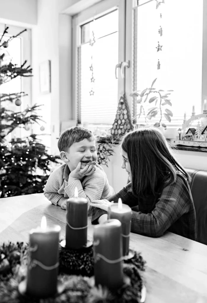 Zwei Kinder sitzen lachend am Tisch hinter einem Adventskranz