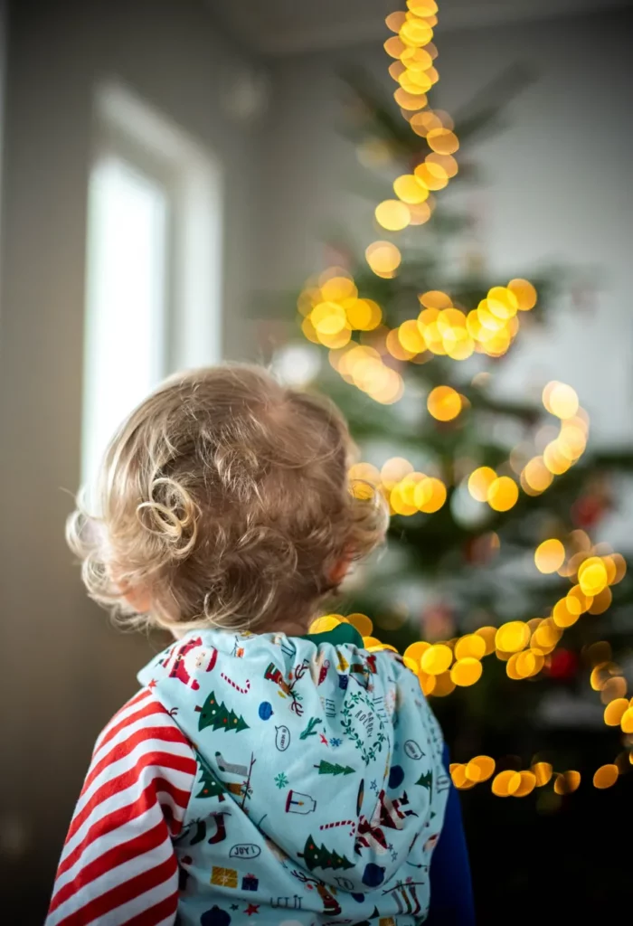 Kleinkind schaut von hinten auf die leuchtenden Lichter des Weihnachtsbaums