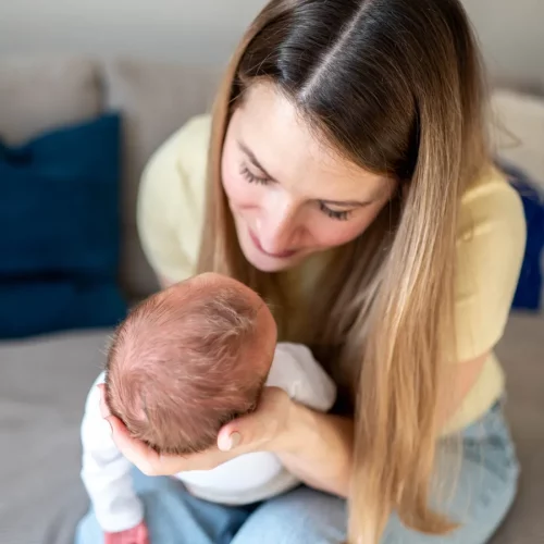 Mutter hält ihr Neugeborenes liebevoll bei einem natürlichen Babyfotoshooting zuhause